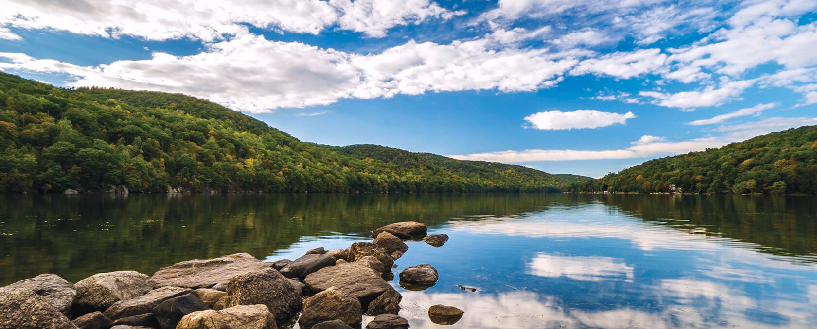 mountain lake with rock jetty and forest in New England Candlewood Lake in Connecticut with reflections and sky during fall